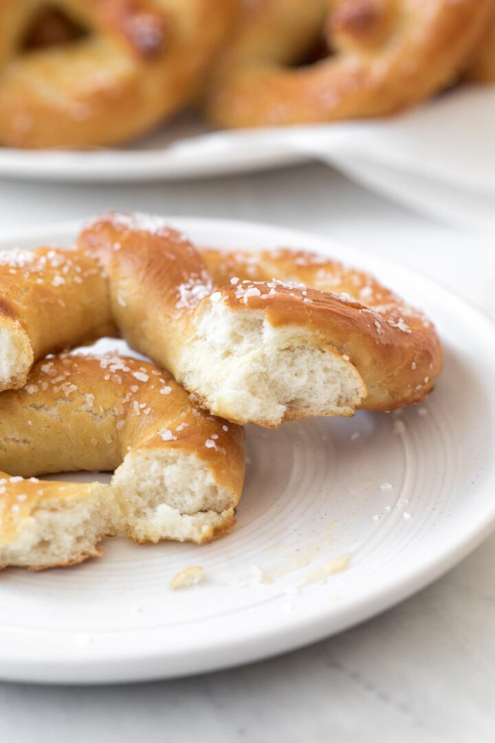 A broken piece of a homemade soft pretzel showing the soft, fluffy interior on a white plate.