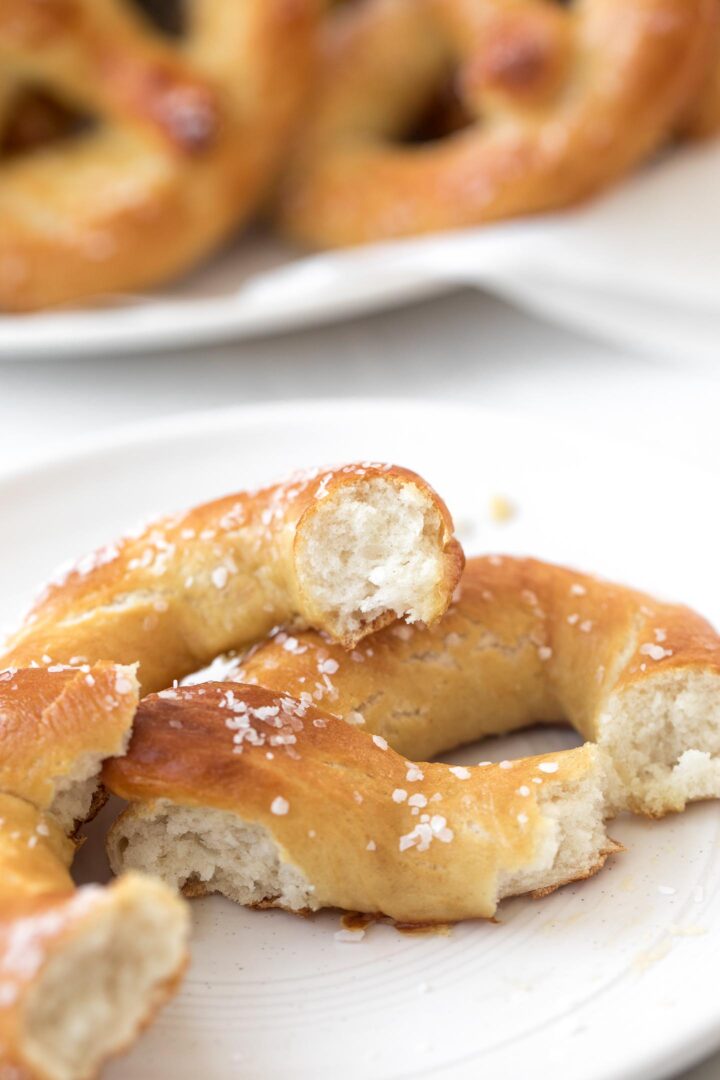 A broken piece of a homemade soft pretzel showing the soft, fluffy interior on a white plate.