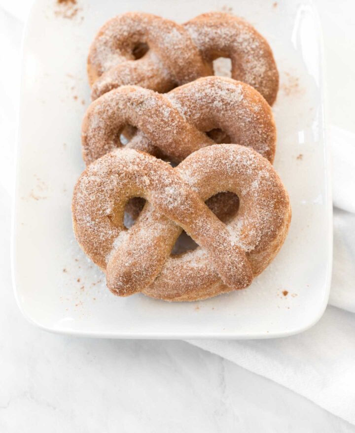 Three soft cinnamon sugar pretzels on a white, rectangular plate.