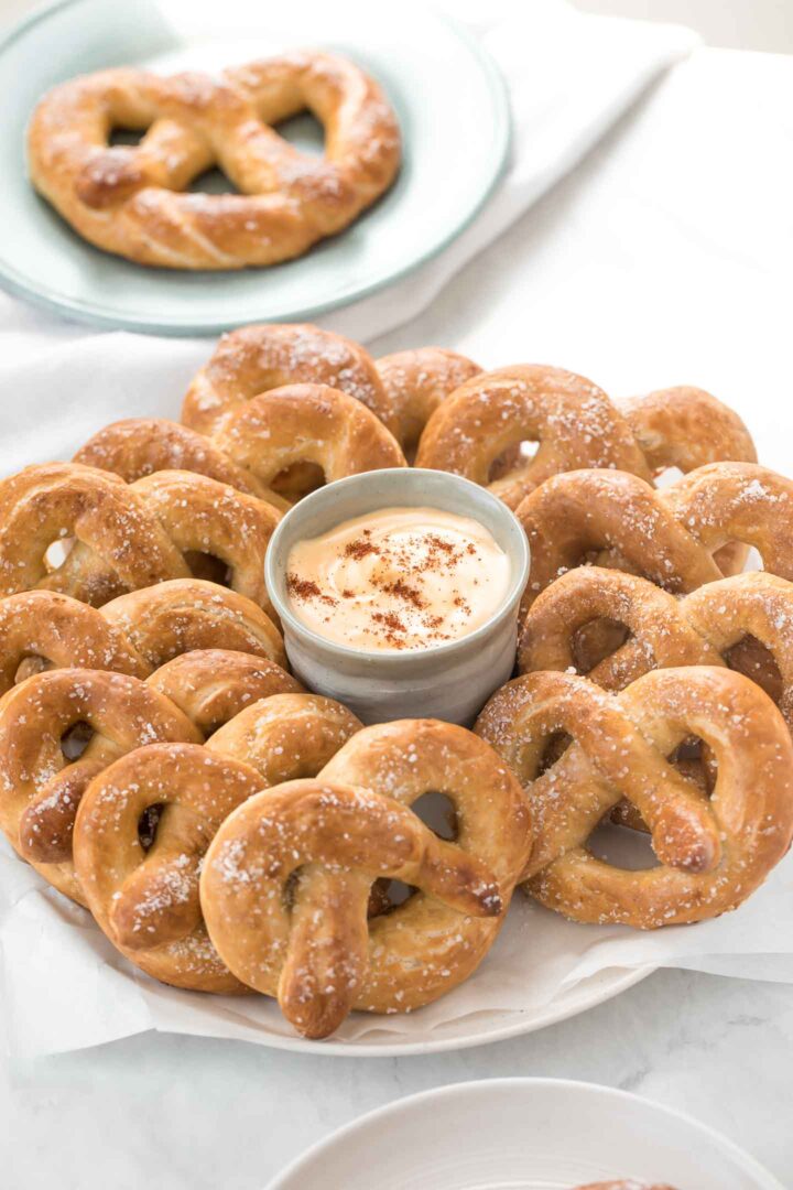 A plate of multiple homemade soft pretzels with a cheese dip in a green bowl in the center. 