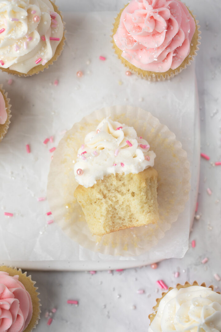Vanilla Cupcakes with Buttercream Frosting with pink sprinkles with a bite taken out of it.