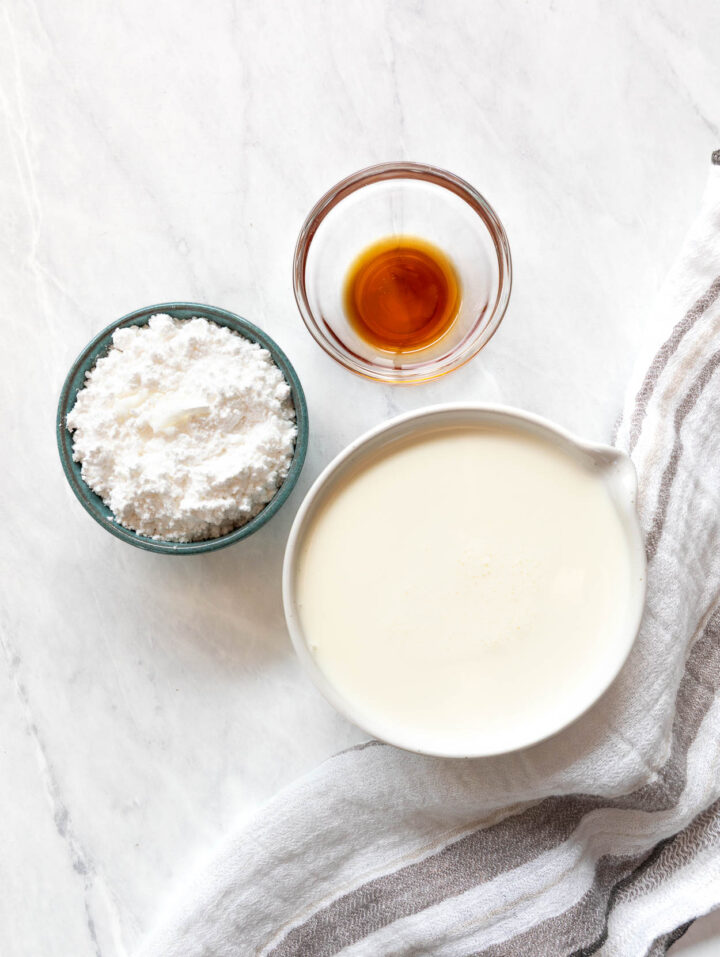 Heavy cream, vanilla extract and confectioner's sugar in bowls.