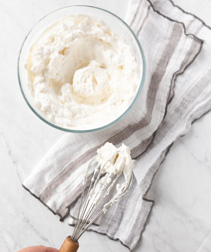 Whipped Cream in a bowl with whipped cream on a whisk.