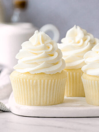 Vanilla cupcakes with buttercream frosting on marble plate.