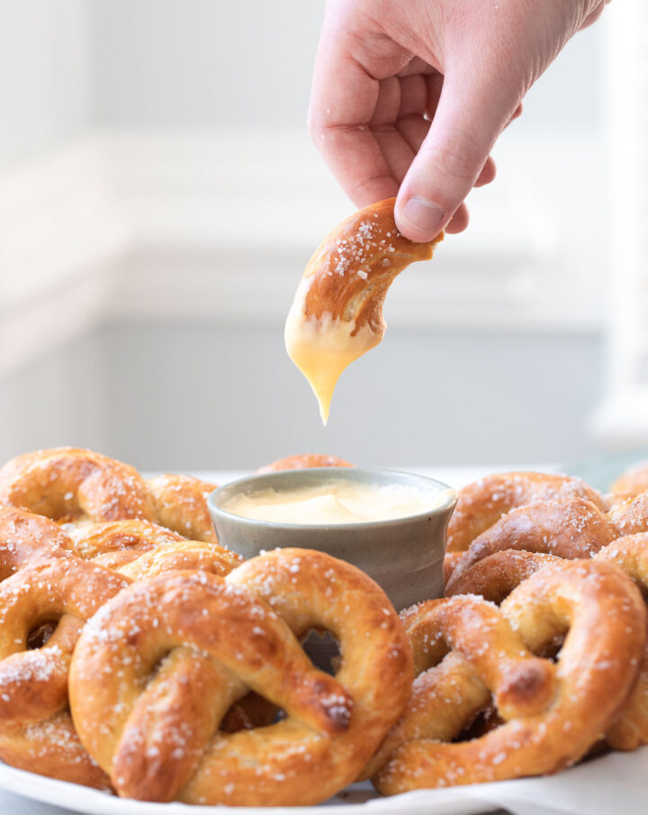 Homemade soft pretzels on a plate with a piece of soft pretzel dipped in cheese sauce.