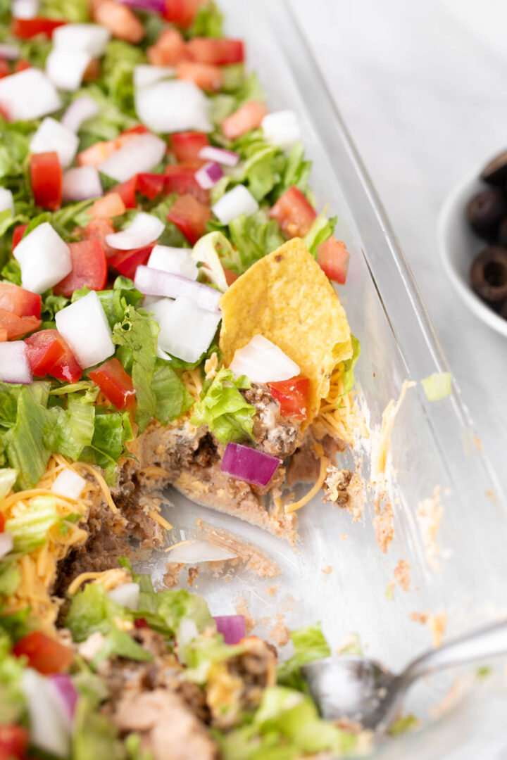 7 layer dip in a glass baking dish with a tortilla scooping the dip
