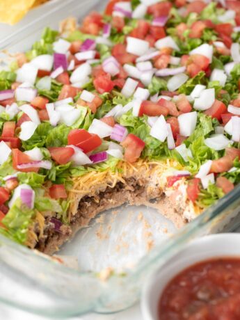7 layer dip in a glass baking dish topped with shredded lettuce, diced tomato and onion.