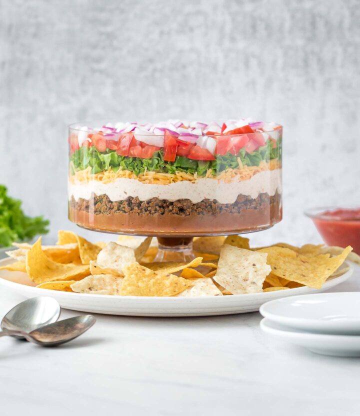 7 layer dip in a glass bowl on a tray with tortillas