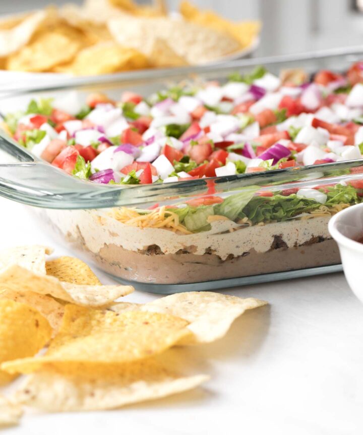 7 Layer Dip in a glass baking dish with a bowl of tortilla chips
