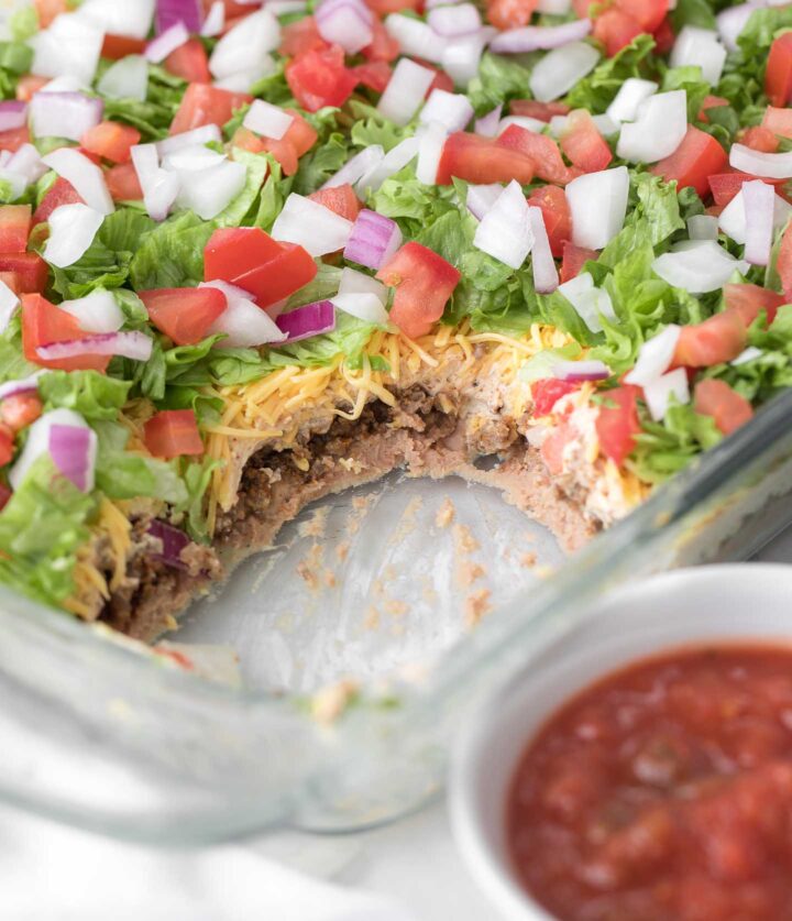 7 layer dip in a glass baking dish topped with shredded lettuce, diced tomato and onion.
