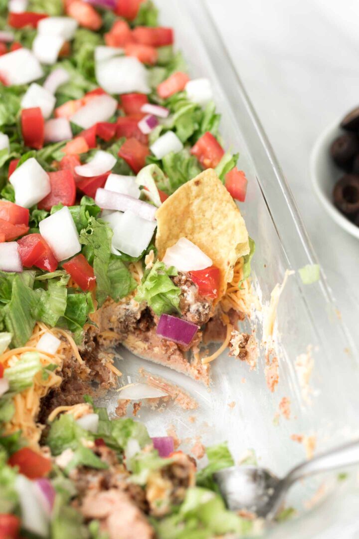 7 layer dip in a glass baking dish with a tortilla scooping the dip