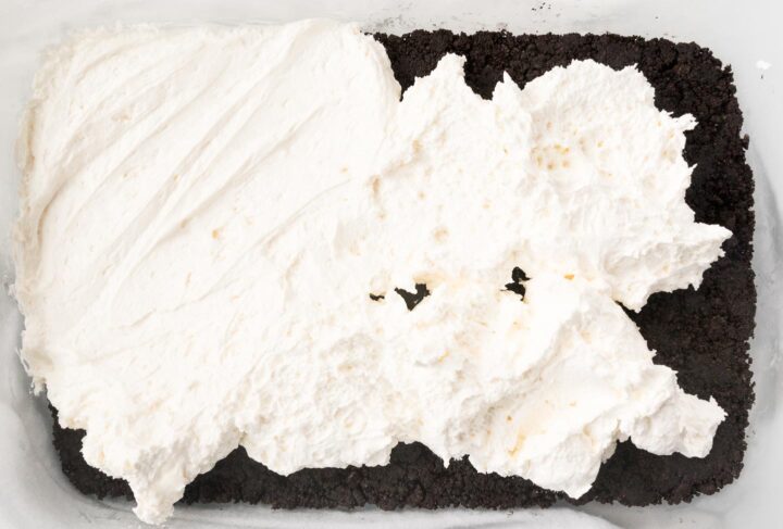 Cream cheese and Cool Whip being spread over an Oreo cookie crust in a baking dish.