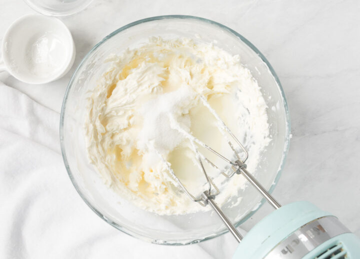 Cream cheese, sugar and milk whipped together with a hand held mixer in a clear bowl.