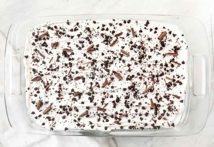 Chocolate lasagna topped with mini chocolate chips, crushed Oreo cookies and chocolate shavings in a 9x13 clear baking dish.