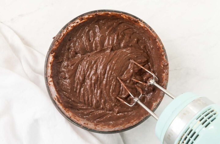 Chocolate pudding being mixed with a hand held mixer in a medium sized bowl.