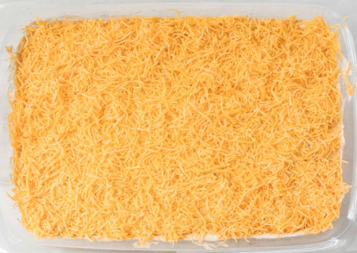 Shredded cheddar cheese spread out onto a 9x13 baking dish.