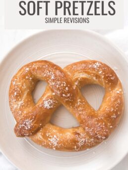 A soft pretzel with butter and coarse salt on a white plate.