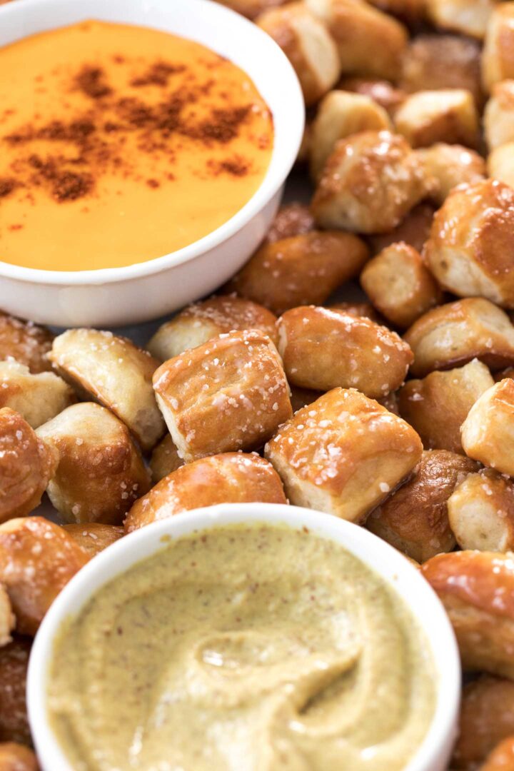 soft pretzel bites on a baking sheet with nacho cheese sauce and spicy mustard in a white bowl