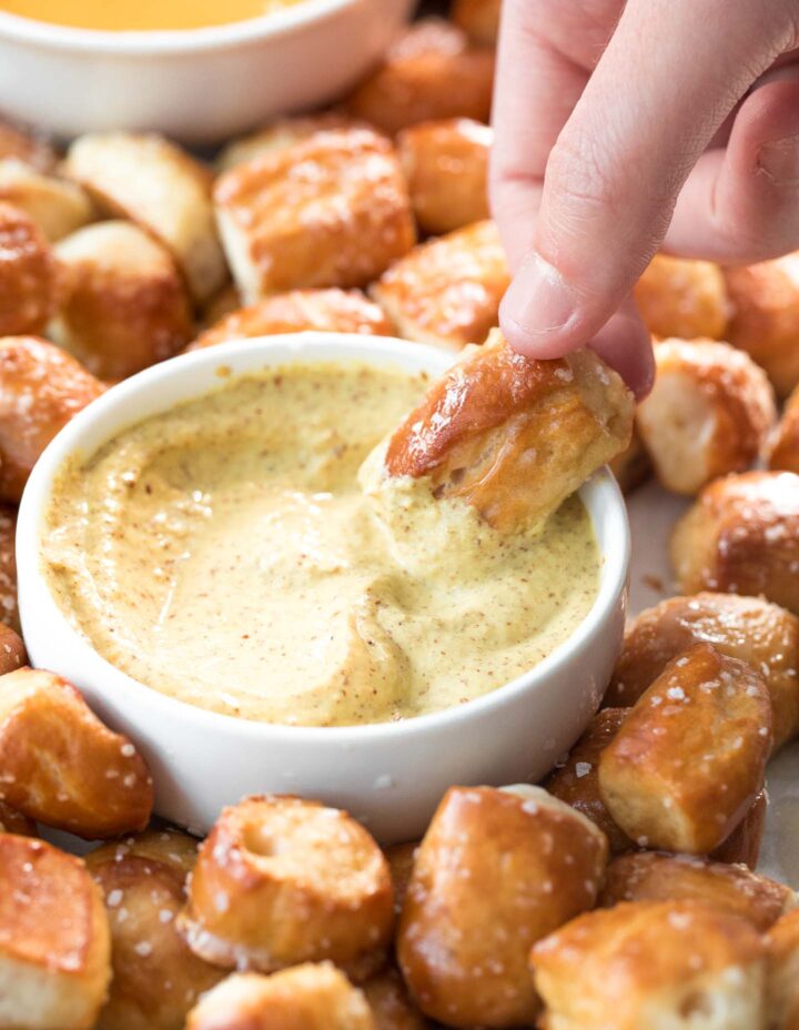 a soft pretzel bite dipped into a small white bowl of spicy mustard