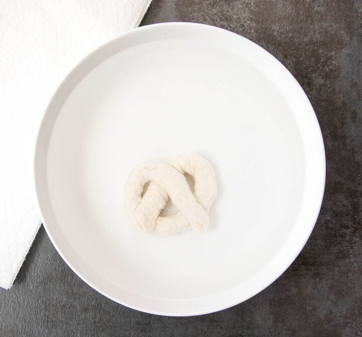 Soft pretzel dough in a white bowl for a baking soda bath.