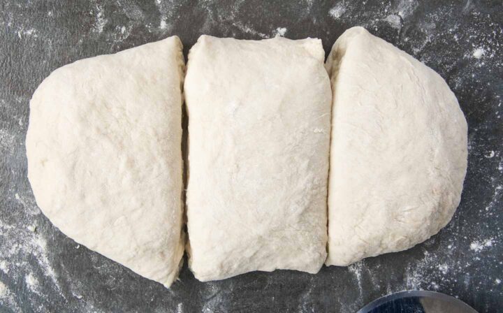 Pretzel dough divided into three equal pieces on a floured surface.