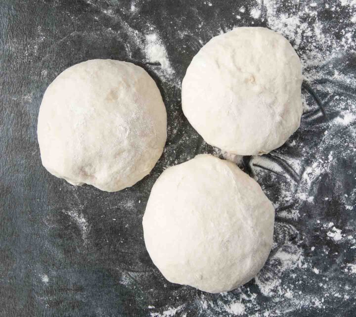 Three balls of dough on a floured surface.