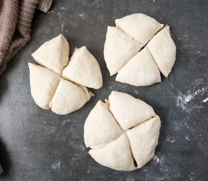 Three balls of soft pretzel dough on a floured surface. Each ball of dough is divided into four individual pieces for a total of 12 sections.